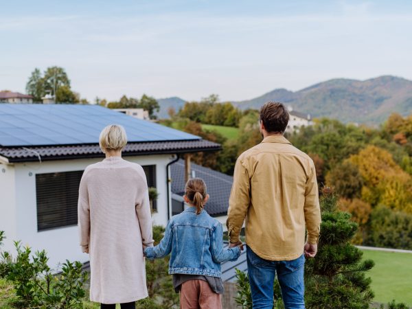 Rear view of family looking at their house with solar panels.Alternative energy, saving resources and sustainable lifestyle concept.