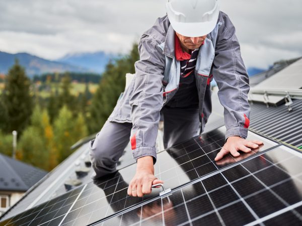 Man engineer mounting photovoltaic solar panels on roof of house. Technician in helmet installing solar module system with help of hex key. Concept of alternative, renewable energy.